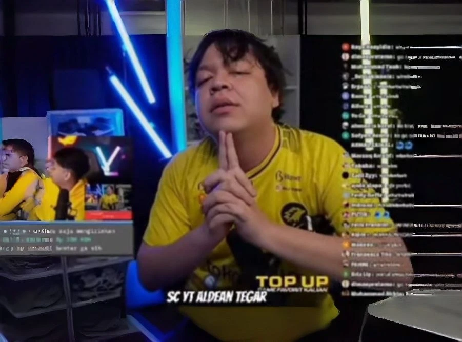Pria berjersey kuning menopang dagu dengan kedua tangan di depan latar neon biru